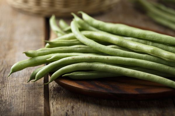 Photo of a pile of green beans on a wooden plate. 